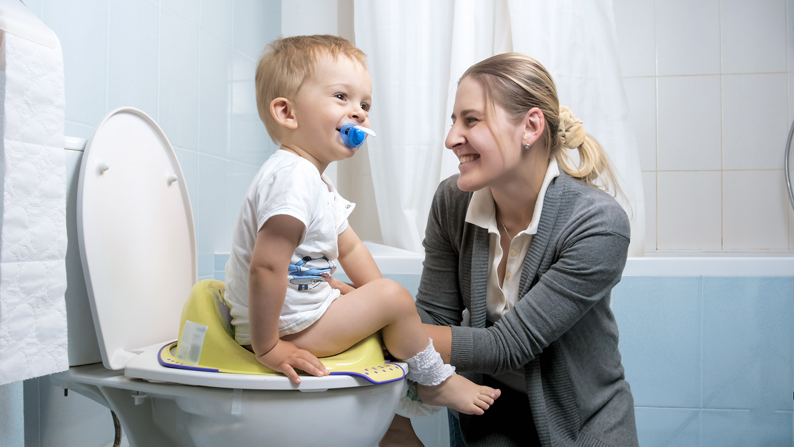 Cute little boy smiling to mother while sitting on toilet seat